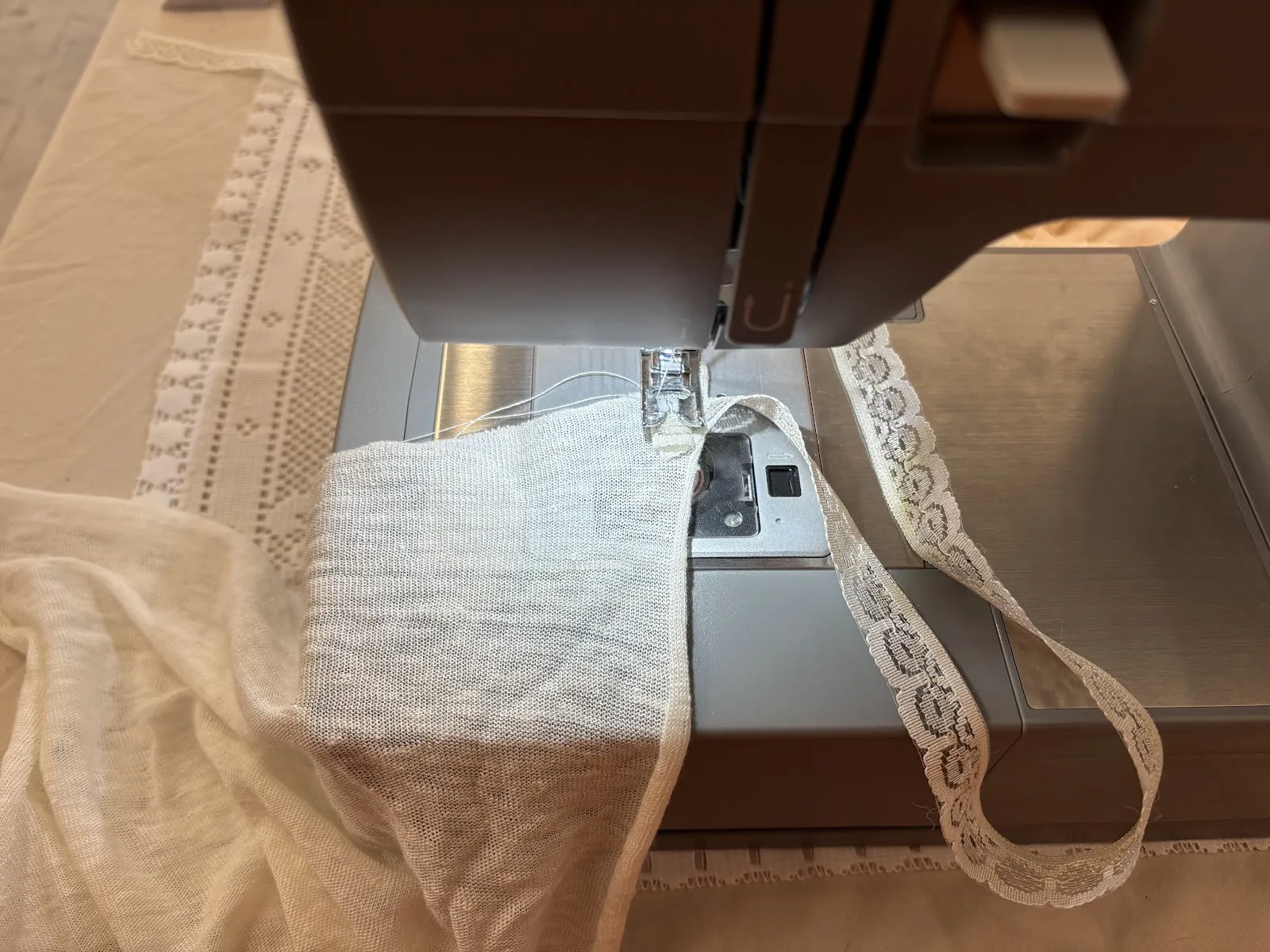 White fabric and lace under the foot of a sewing machine